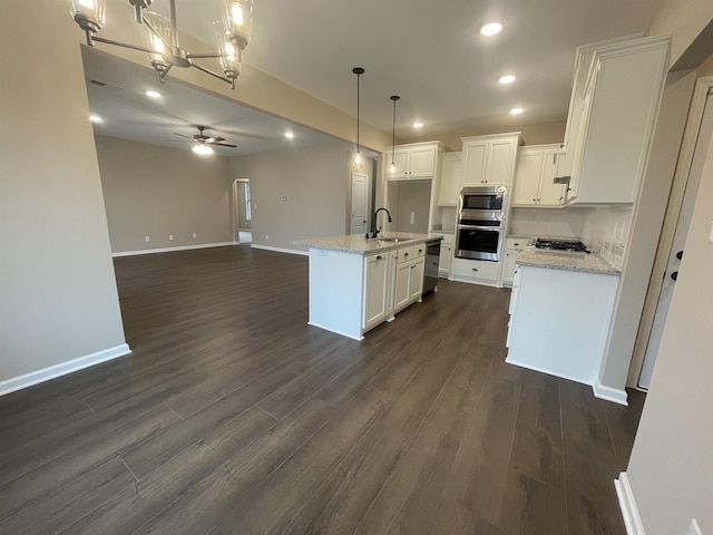 kitchen with a center island with sink, white cabinets, open floor plan, hanging light fixtures, and stainless steel appliances