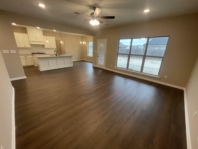 unfurnished living room with baseboards, a ceiling fan, dark wood-style flooring, and a sink