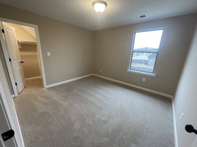 unfurnished bedroom with a walk in closet, light carpet, visible vents, and baseboards