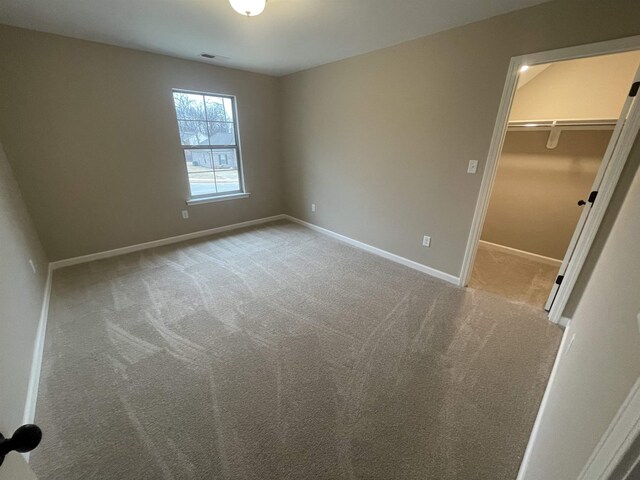 unfurnished bedroom featuring light carpet, a walk in closet, visible vents, and baseboards