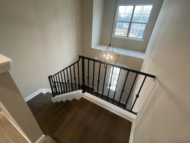 stairs featuring a chandelier, wood finished floors, a towering ceiling, and baseboards