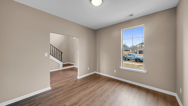 spare room featuring visible vents, dark wood finished floors, baseboards, and stairs