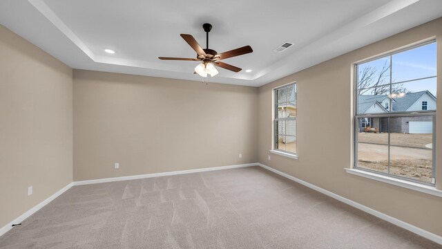 empty room featuring a healthy amount of sunlight, visible vents, a tray ceiling, and baseboards