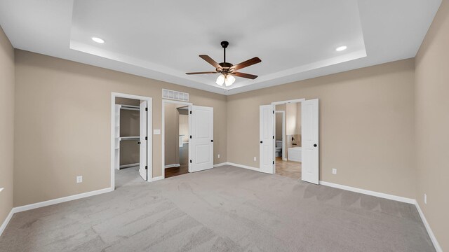 unfurnished bedroom with a tray ceiling, visible vents, a spacious closet, and baseboards