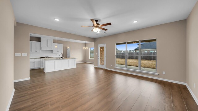 unfurnished living room featuring dark wood-style floors, baseboards, and ceiling fan with notable chandelier