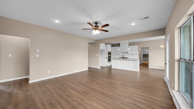 unfurnished living room featuring dark wood-style flooring, a sink, visible vents, baseboards, and a ceiling fan