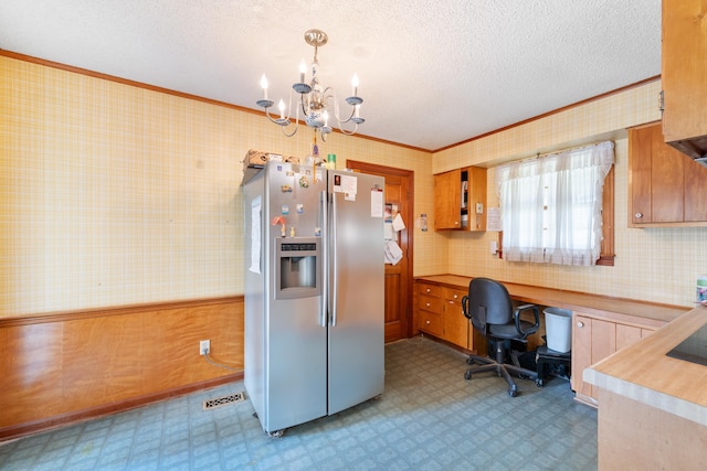 kitchen with stainless steel fridge, ornamental molding, decorative light fixtures, built in desk, and a chandelier