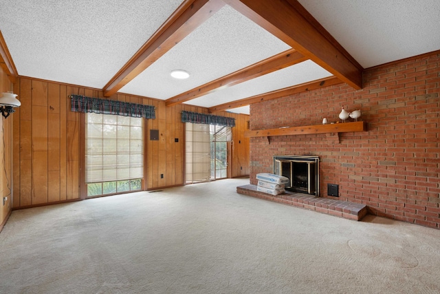 unfurnished living room with beam ceiling, a textured ceiling, wooden walls, carpet floors, and a fireplace