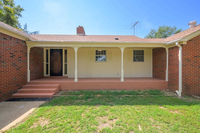 view of exterior entry with a lawn and covered porch