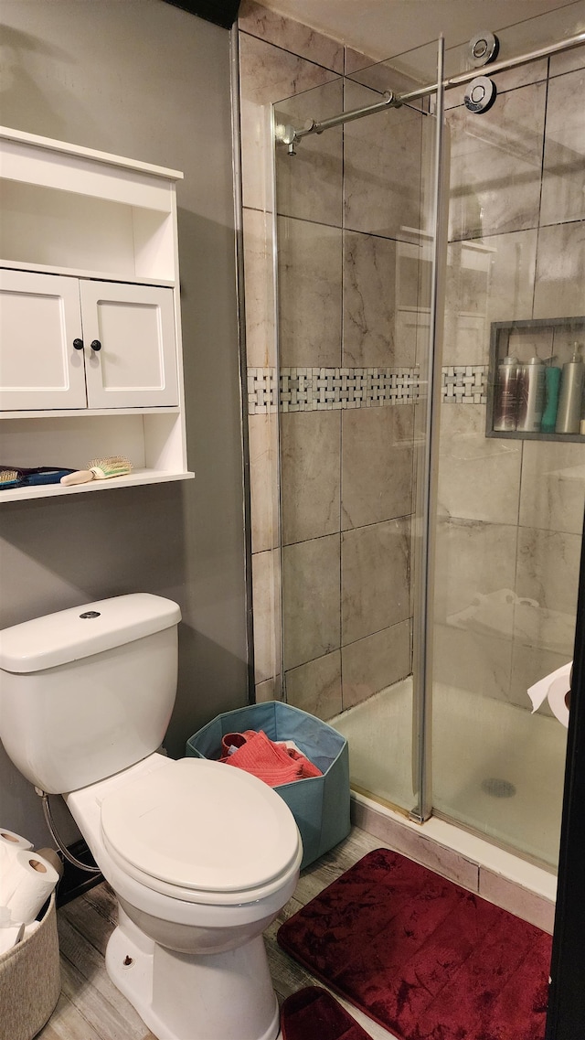 bathroom with hardwood / wood-style floors, a shower with door, and toilet