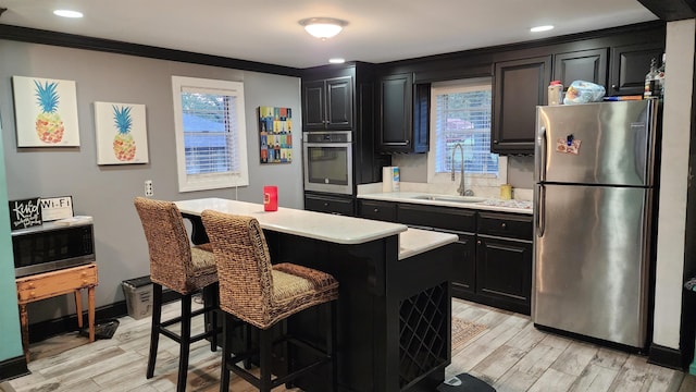 kitchen with appliances with stainless steel finishes, a kitchen breakfast bar, light hardwood / wood-style floors, a kitchen island, and sink