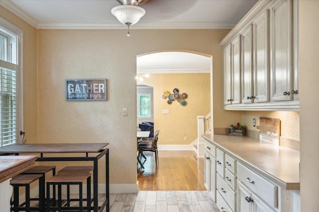 kitchen with crown molding, light hardwood / wood-style floors, white cabinets, and a wealth of natural light