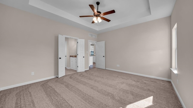 unfurnished bedroom featuring ceiling fan, a raised ceiling, and light colored carpet