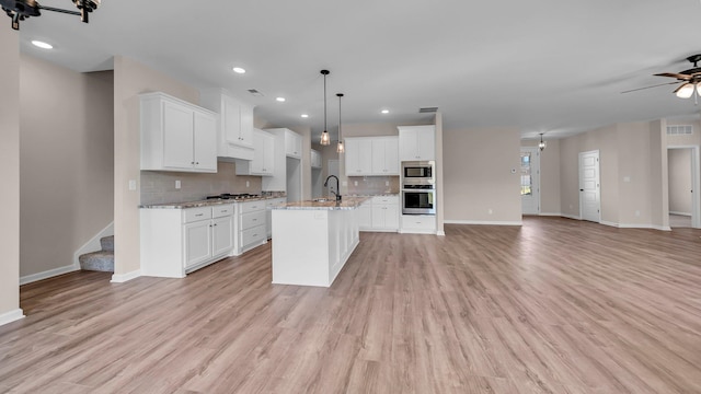 kitchen with a kitchen island with sink, hanging light fixtures, light hardwood / wood-style floors, white cabinetry, and stainless steel appliances