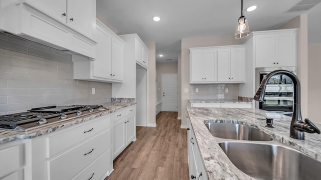 kitchen with backsplash, sink, light hardwood / wood-style floors, white cabinetry, and stainless steel gas stovetop