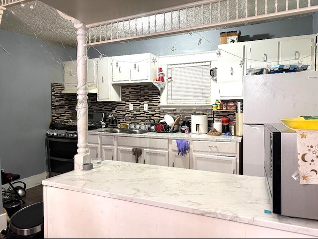 kitchen with sink, tasteful backsplash, black range, white cabinetry, and light stone countertops