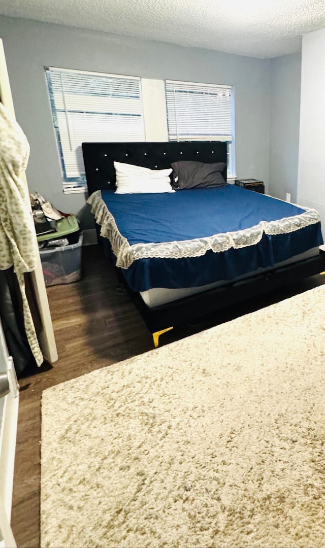 bedroom featuring multiple windows, a textured ceiling, and dark hardwood / wood-style floors