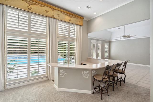 kitchen featuring kitchen peninsula, a kitchen bar, ceiling fan, ornamental molding, and light colored carpet