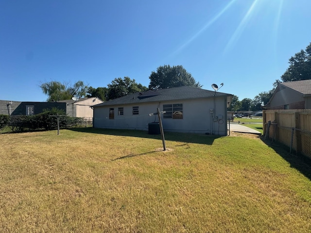 rear view of house featuring central AC unit, fence, and a yard