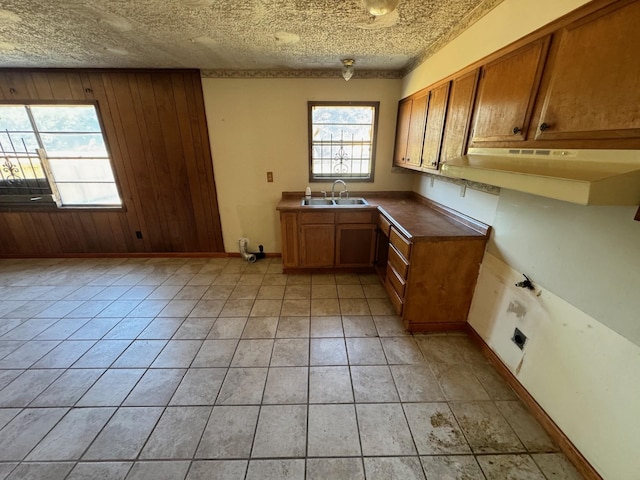 kitchen featuring a textured ceiling, light tile patterned flooring, wooden walls, and sink