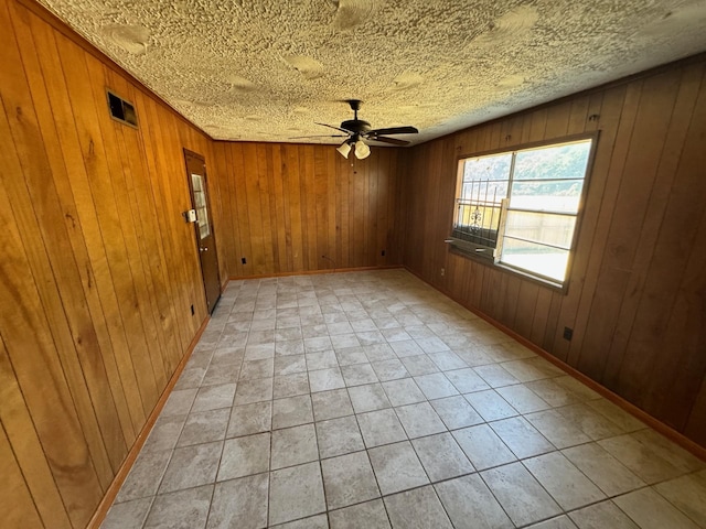 unfurnished room featuring baseboards, wooden walls, visible vents, and ceiling fan