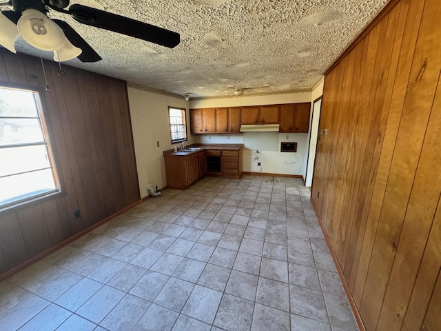 kitchen featuring brown cabinets, wooden walls, a sink, light tile patterned floors, and ceiling fan