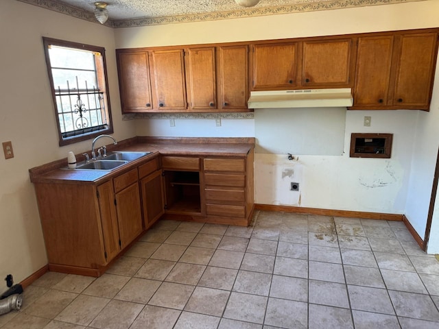 kitchen with brown cabinetry, baseboards, under cabinet range hood, and a sink