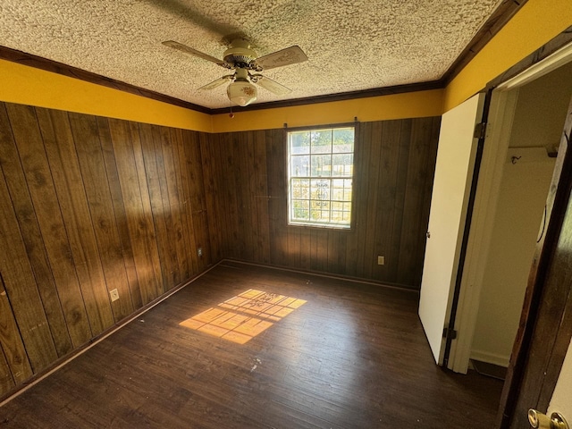 unfurnished bedroom featuring dark hardwood / wood-style flooring, a textured ceiling, wooden walls, ceiling fan, and ornamental molding