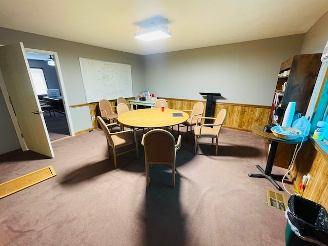 dining space featuring carpet flooring, wooden walls, and a wood stove