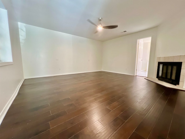 unfurnished living room with ceiling fan, dark wood-type flooring, and a tile fireplace