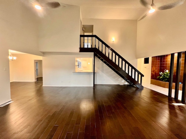 unfurnished living room featuring dark wood-type flooring, ceiling fan with notable chandelier, and a high ceiling