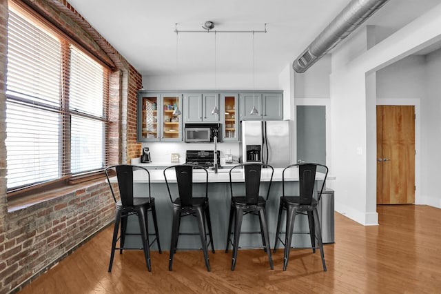 kitchen featuring gray cabinets, wood-type flooring, a wealth of natural light, appliances with stainless steel finishes, and brick wall