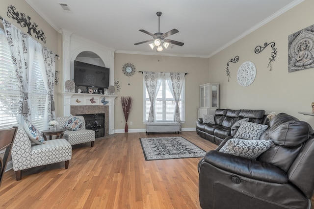 living room featuring wood-type flooring, a tiled fireplace, ceiling fan, and crown molding