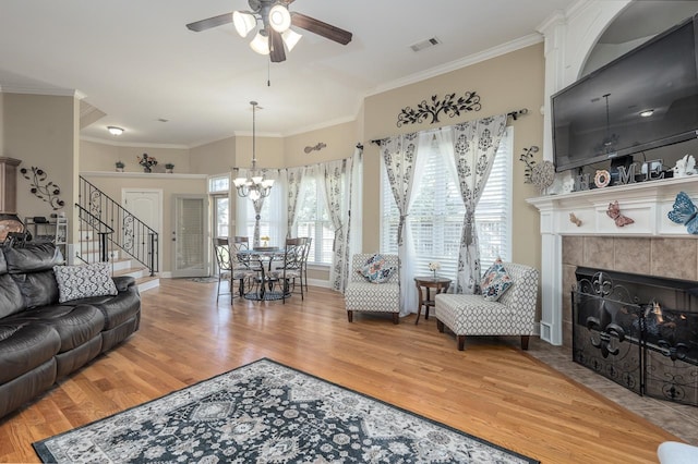 living room featuring light hardwood / wood-style flooring, a tiled fireplace, ceiling fan with notable chandelier, and crown molding