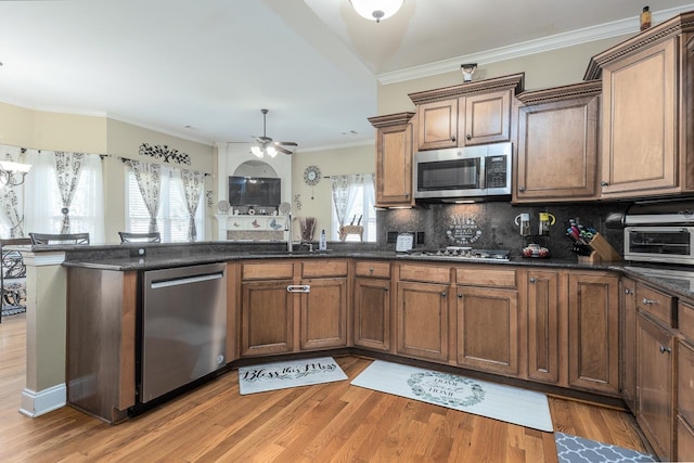 kitchen with backsplash, stainless steel appliances, light wood-type flooring, ceiling fan, and ornamental molding