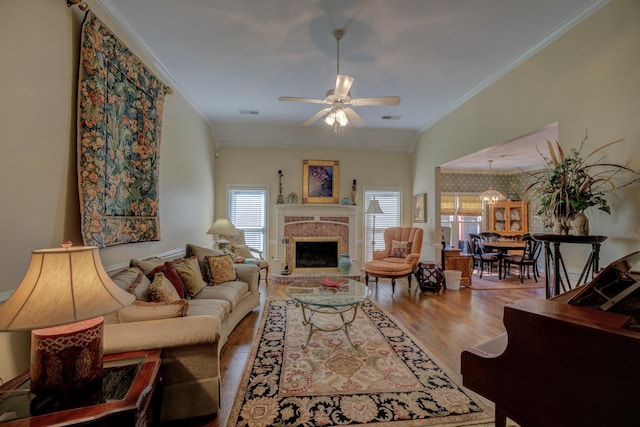 living room featuring ceiling fan, hardwood / wood-style flooring, a brick fireplace, and ornamental molding