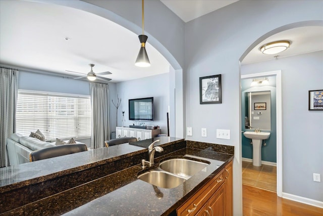 kitchen featuring hanging light fixtures, dark stone countertops, light wood-type flooring, ceiling fan, and sink