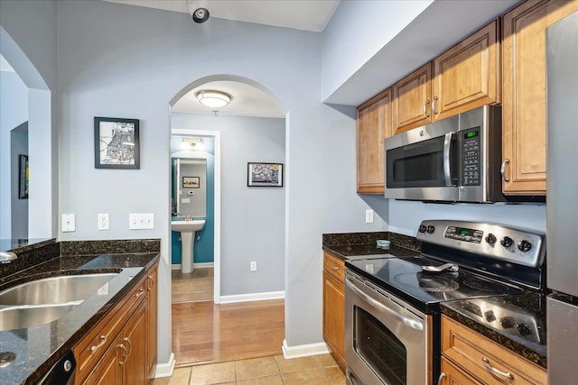 kitchen with dark stone countertops, light tile patterned flooring, sink, and stainless steel appliances