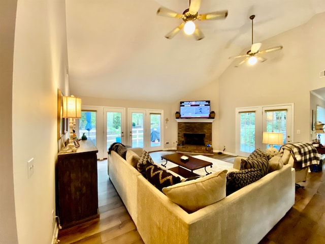 living area featuring baseboards, a ceiling fan, wood finished floors, a brick fireplace, and high vaulted ceiling