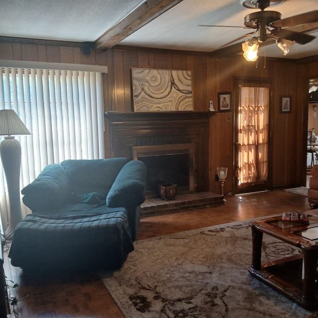 living room with a brick fireplace, beamed ceiling, wooden walls, and ceiling fan