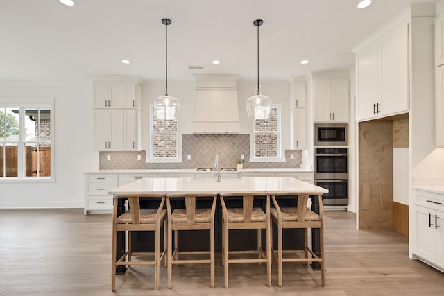 kitchen with an island with sink, white cabinetry, hardwood / wood-style floors, and decorative light fixtures