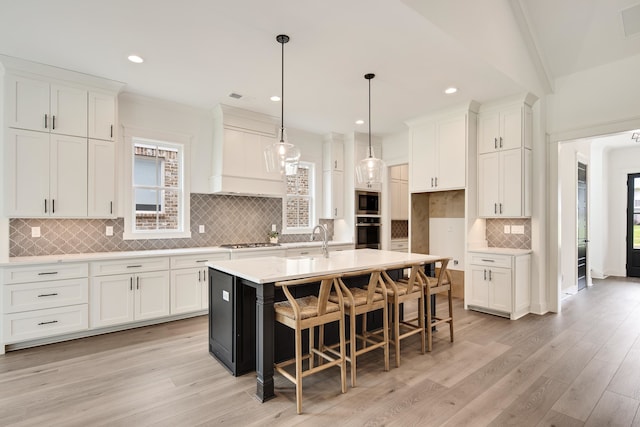 kitchen featuring decorative backsplash, light wood-type flooring, and a center island with sink