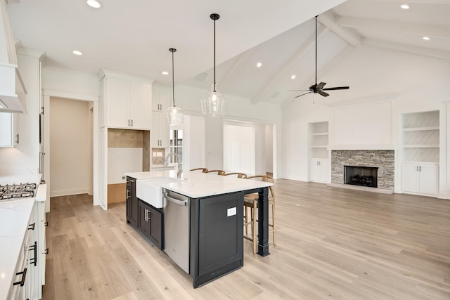 kitchen featuring ceiling fan, hanging light fixtures, stainless steel dishwasher, a kitchen island with sink, and a fireplace