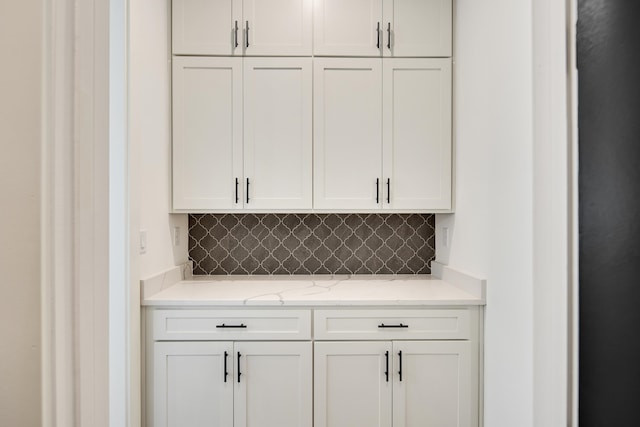 bar featuring tasteful backsplash, light stone countertops, and white cabinets