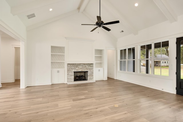 unfurnished living room featuring light hardwood / wood-style floors, beamed ceiling, high vaulted ceiling, a stone fireplace, and ceiling fan