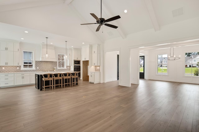 unfurnished living room with ceiling fan with notable chandelier, light hardwood / wood-style floors, beam ceiling, and high vaulted ceiling