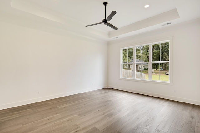 empty room with ceiling fan, a tray ceiling, and light hardwood / wood-style flooring