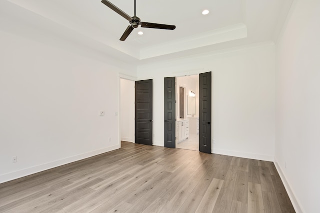 unfurnished bedroom with a tray ceiling, light hardwood / wood-style floors, ensuite bath, ornamental molding, and ceiling fan