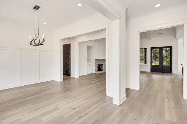 spare room featuring light wood-type flooring, a stone fireplace, ornamental molding, and a chandelier