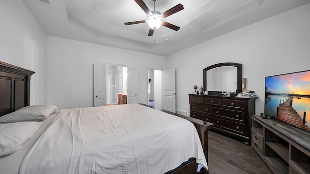 bedroom featuring dark hardwood / wood-style flooring, ensuite bathroom, ceiling fan, and a tray ceiling